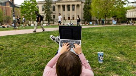 Student laying down on the main quad with a laptop placed on their legs.